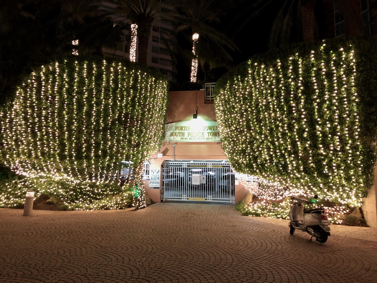 Condominium entrance lighting Vertical white light strands cover hedges on both sides of a condominium entrance.